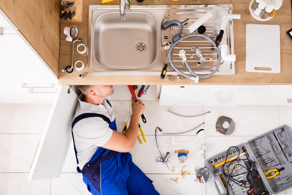 High,Angle,View,Of,Male,Plumber,In,Overall,Fixing,Sink
